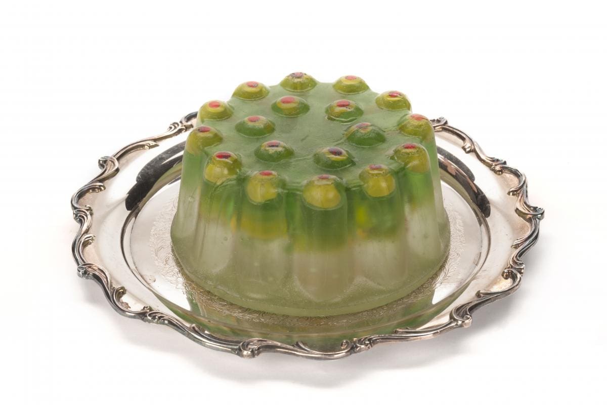 Glass sculpture in the shape of a gelatin cake with olives at the top. On a silver platter.
