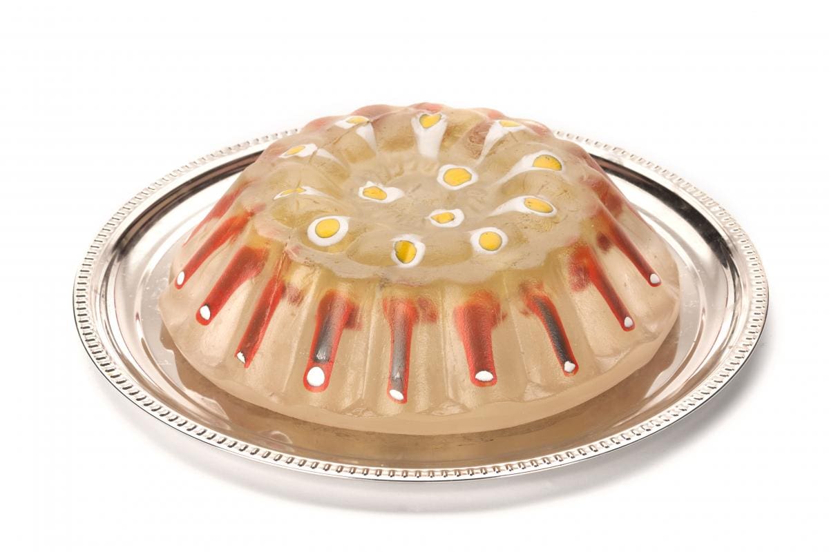 Glass sculpture that looks like a mold of jello with eggs and sausage inside. On a silver platter.