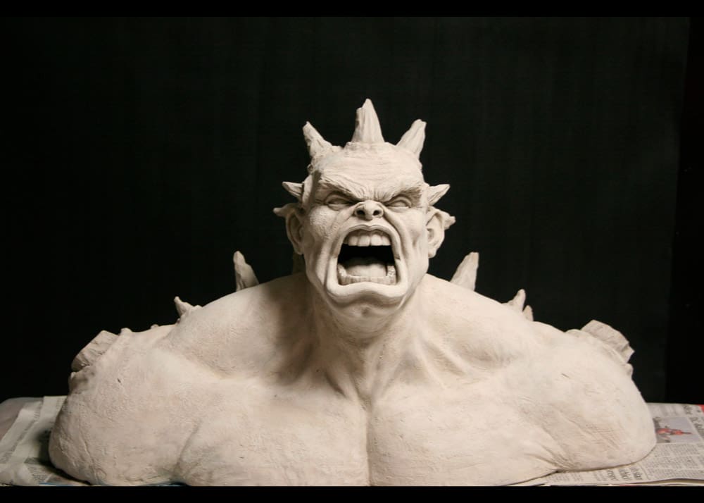 Gabriel Vinas. Ceramic sculpture on a black background. depicts the top half of a muscular, sreaming, ogre-like character with horns going down its shoulders and on top of its head.
