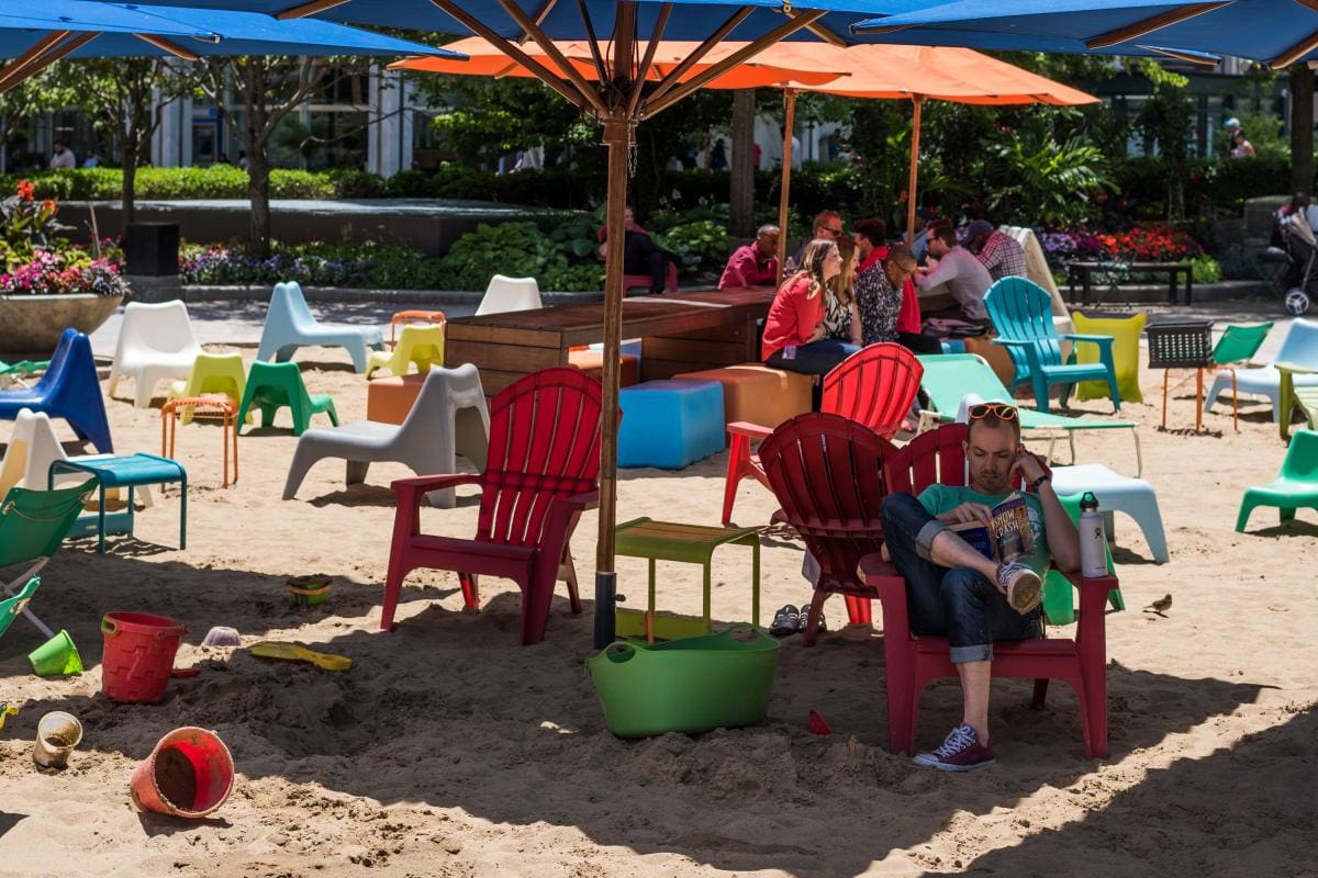 Photo of people sitting on dec chairs under umbrellas on a plot of sand in Detroit.