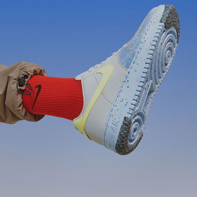 Photo of a leg with brown baggy pants, red socks, and blue sneakers with yellow details. The background is blue