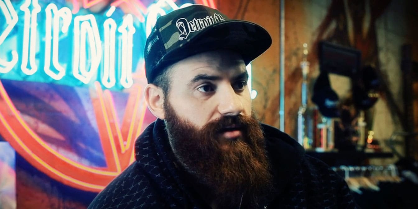 Headshot of a bearded man looking slightly to the right. The background has a huge blue and red neon sign