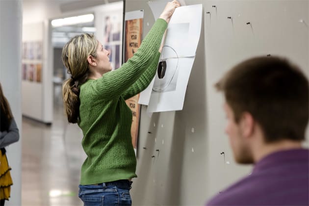 a student pinning her work to a wall
