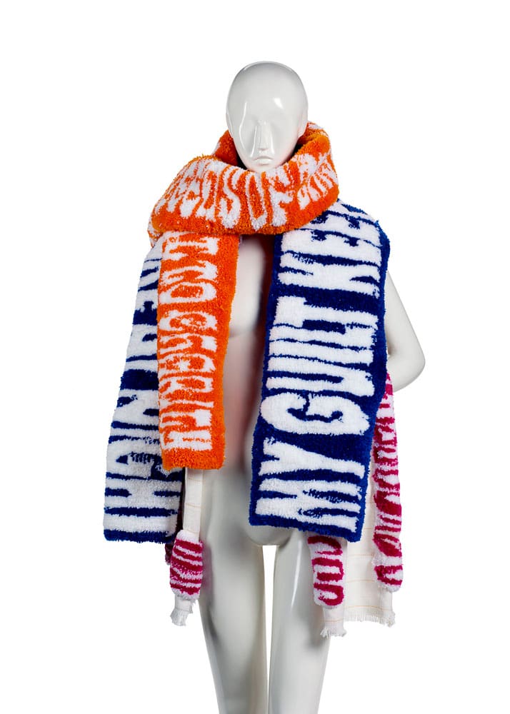 Three rugs scarf. A photograph of a mannequin wearing three fuzzy scarves with text weaved into them.