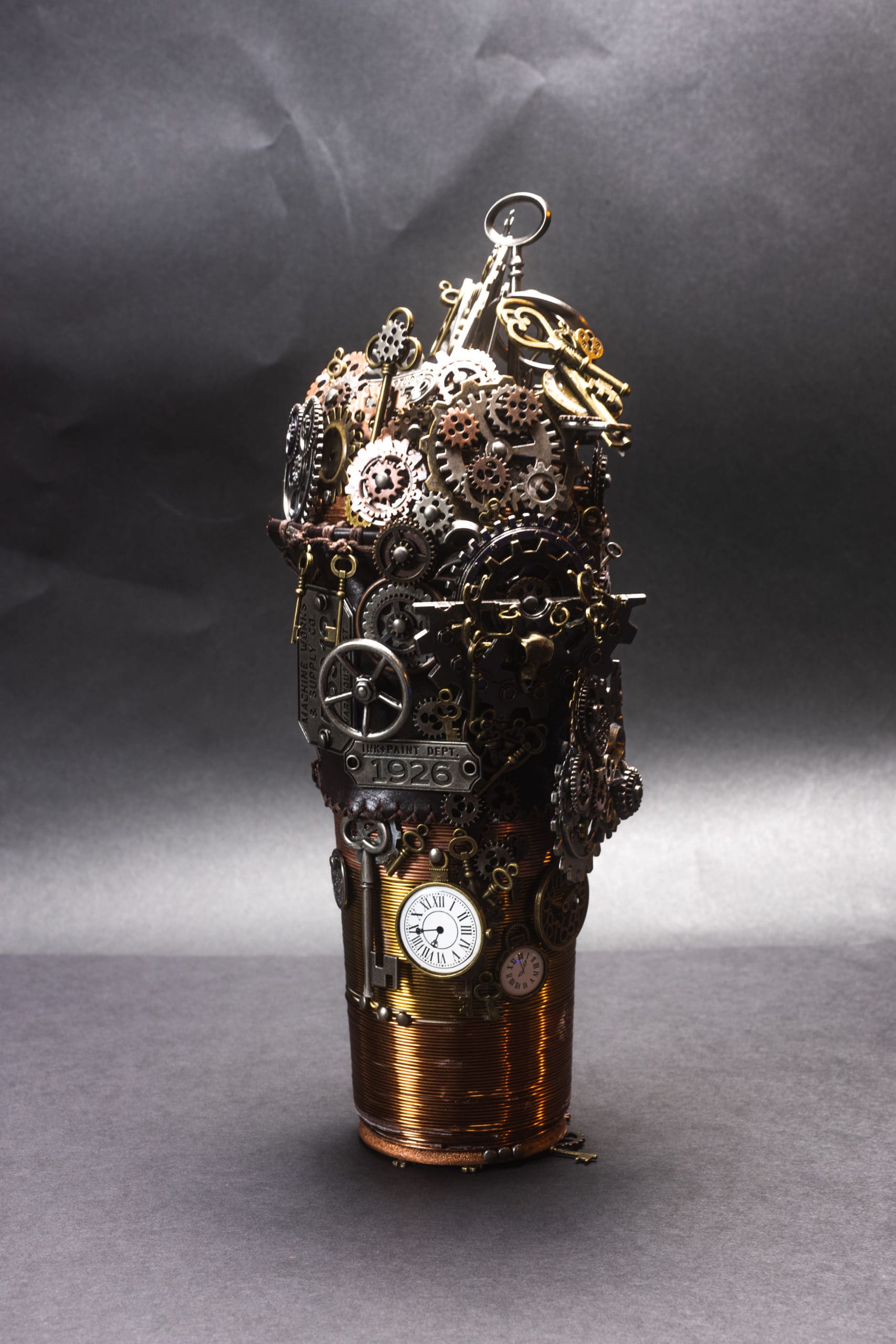 A "Steampunk" take on coffee to go. Cylinder wrapped in copper wire with stitched leather temperature guard. The top is covered in a foam of mechanical metal gears.