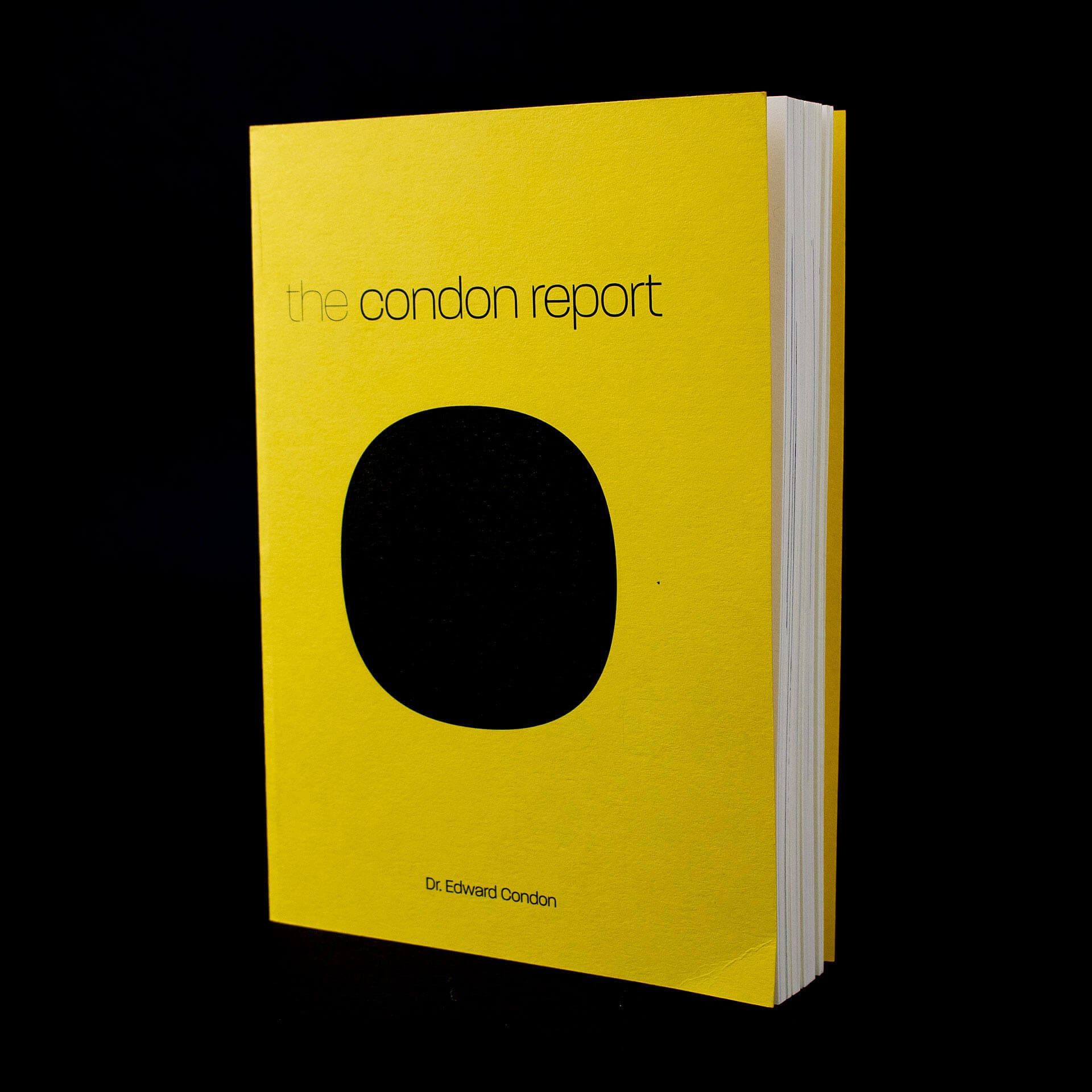 Photo of the book The Condon Report: Scientific Study of Unidentified Flying Objects. Shows a book with a yellow cover with a large black dot in the middle with a thin black title reading "the condon report". Depicted against a black background.
