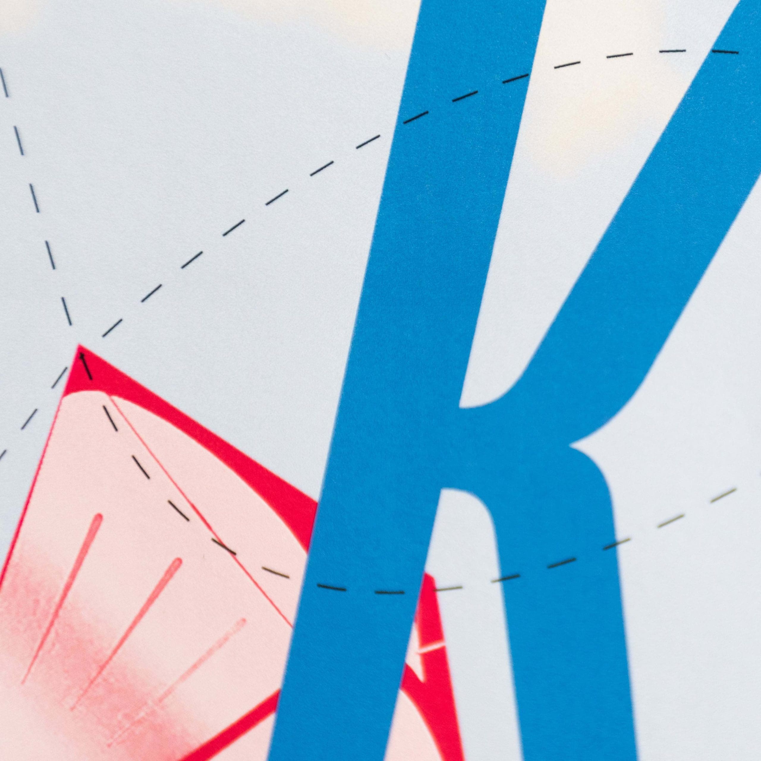 Close-up of a poster that depicts a large blue K spanning from the top to the bottom of the page behind two curved black dashed lines. In the background is a red decorative shape. On a white background.