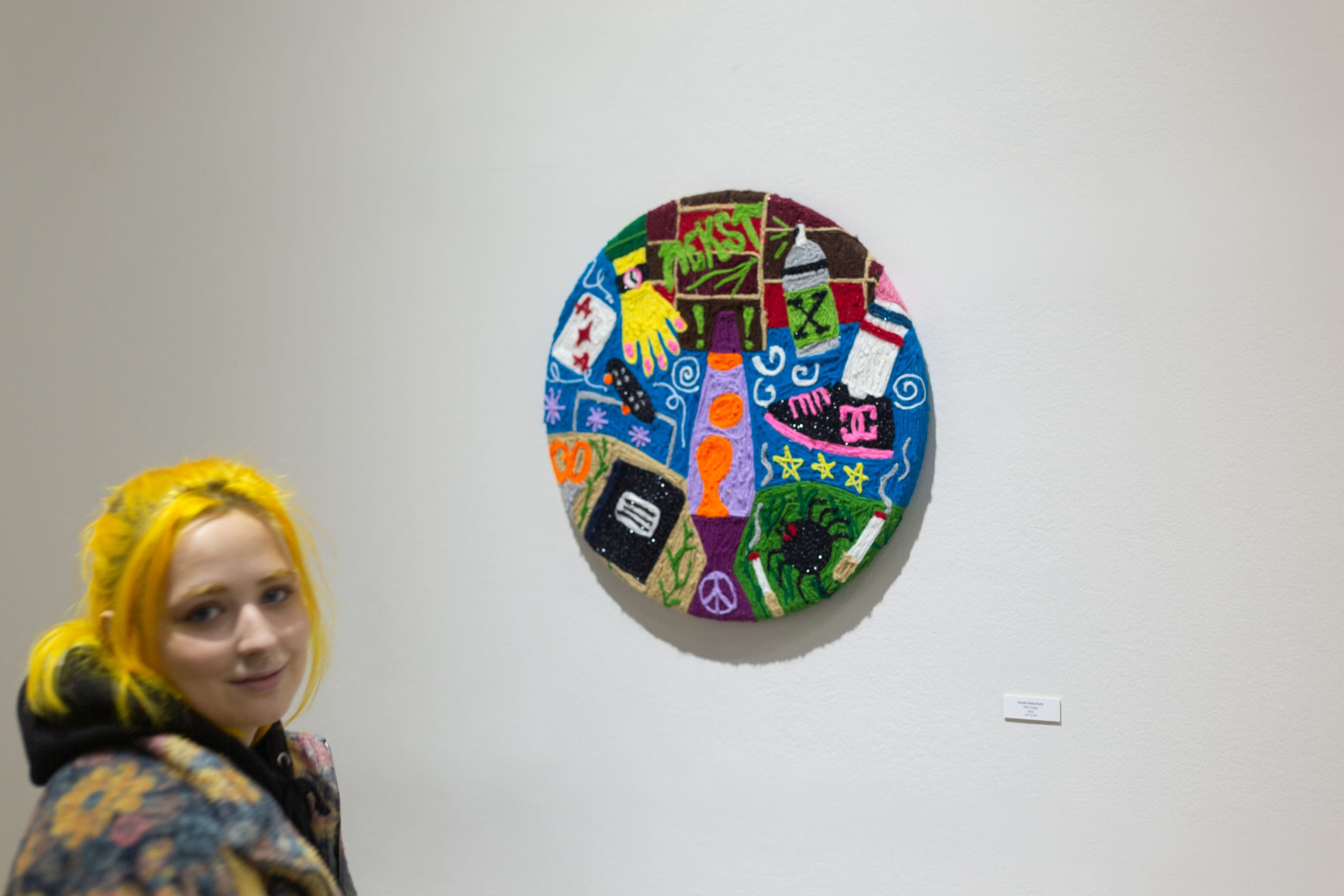 an abstract colorful disc sculpture hanging on a white gallery wall