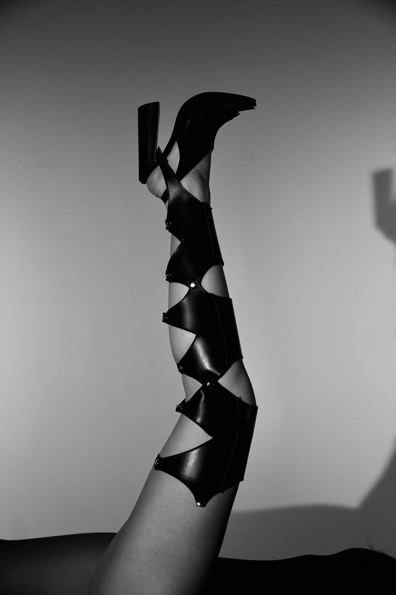 Nikki Park. Black and white photo of a model's leg held in the air, wearing a Modular Boot inspired by the concept of “Han” (Korean Rage). The knee high boot has multiple diamond-shaped cut-outs going up the leg.