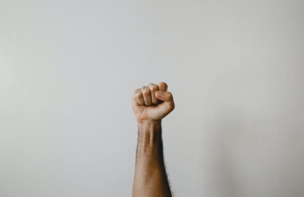a hand with a melanated skin tone holding up a fist against a grey backdrop