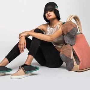 Photo of a sitting model with tan shoes, black kleggings, a white spotted crop top and a black bucket hat. Next to her is a large salmon colored bag.