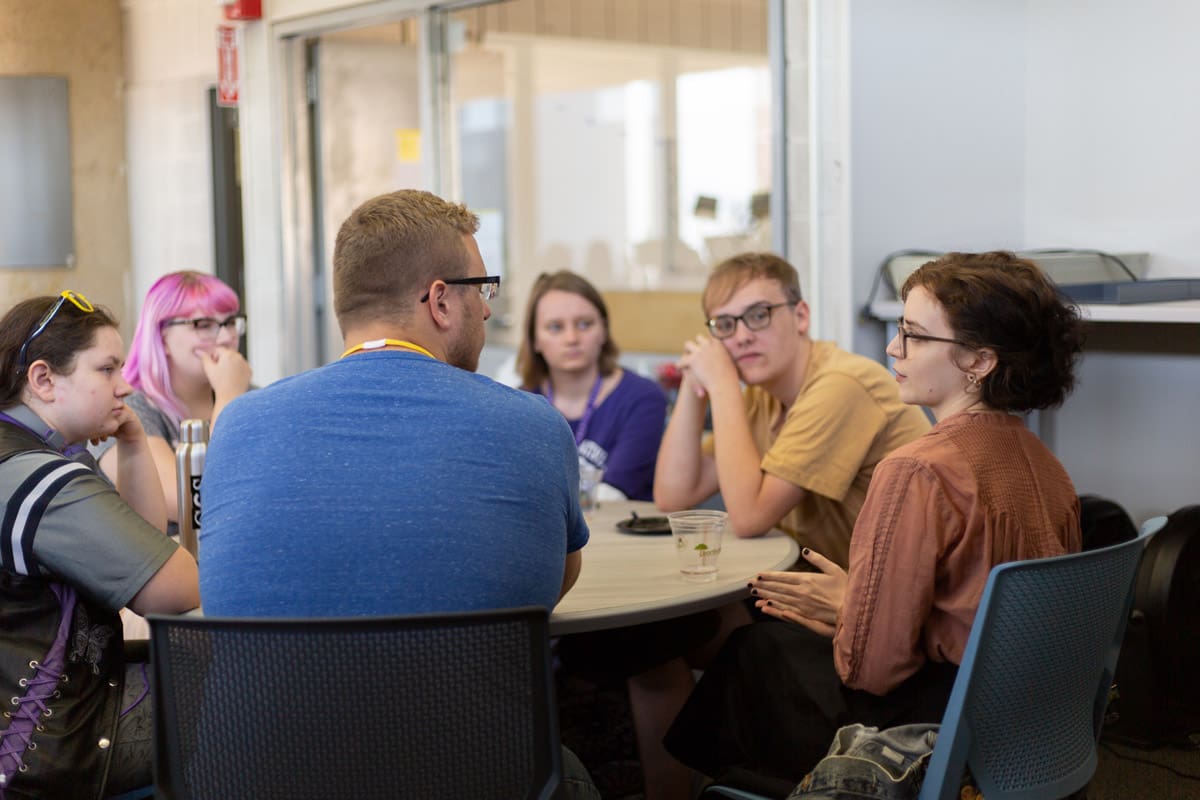 Students sitting and discussing together around a table in the Center for Tutoring room